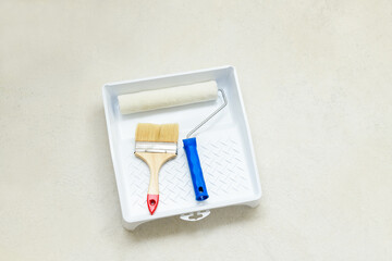 Paint set: roller and brush in tray (bath) on the concrete floor, close-up. Repair tools lies on floor