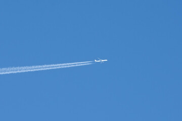 White airplane flies leaving a trail against blue sky.