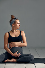 Young pregnant millennial woman sitting on the mat touches her belly after performing prenatal and...