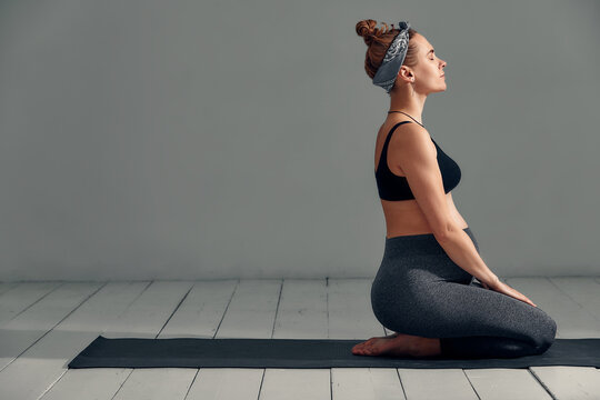 Young pregnant millennial woman sitting on the mat touches her belly after performing prenatal and meditation exercises at a yoga class - Concept of life and maternity
