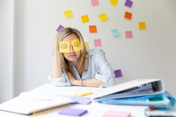 Business woman sits behind her desk on which are many office things and has sticky notes with drawn...