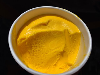Mango ice cream, tropical fruit sorbet in a white paper cup on a black background. Healthy, vegetarian eat, healthy diet food conceptView from above.