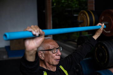 Latin American elderly man and his trainer using a barbell for his rehabilitation and therapy...