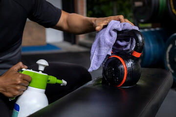 Close-up of a man's hands using a wet wipe and a bottle of disinfectant to clean a kettlebell at...