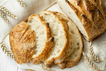 Close up of slices of wheat bread with ears of wheat on linen napkin, view from above, selective focus. Bakery concept.
