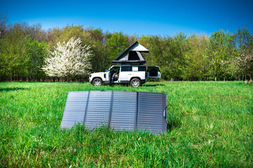 4x4 Offroad vehicle camping with roof tent in a meadwow with solar panel for energy generation in...