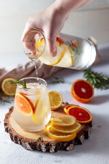 A glass and a decanter of lemonade. Lemon and grapefruit slices with rosemary leaves in a drink