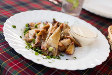 delicious smoked pork ears served with sour cream and herbs on a white plate in a restaurant