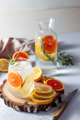 A glass and a decanter of lemonade. Lemon and grapefruit slices with rosemary leaves in a drink