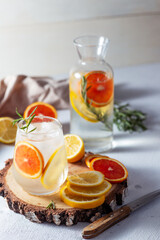 A glass and a decanter of lemonade. Lemon and grapefruit slices with rosemary leaves in a drink