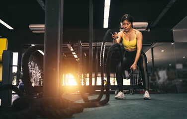 Fototapeta na wymiar Battle ropes session. Attractive young fit and toned Asian sportswoman working out in functional training gym doing crossfit exercise with battle ropes.
