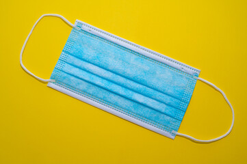 Blue surgical mask, on a yellow surface. Obligation to wear a mask.

