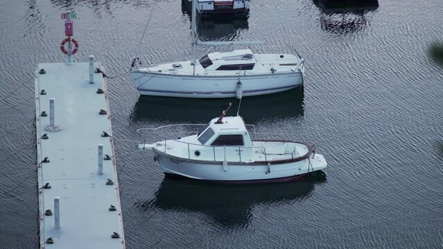 Boats stand at the pier in the port. Small white yachts on dark water. Cloudy day at the boathouse. Sea transport. Marina. The small port in a fishing village. Holidays on the coast. Water ripple.