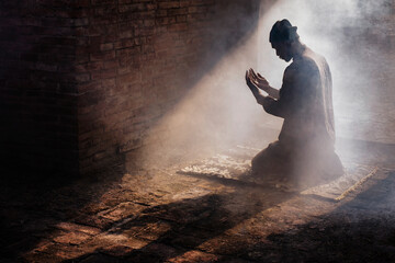 Silhouette of muslim man having worship and praying for fasting and Eid of Islam culture in old mosque with lighting and smoke background