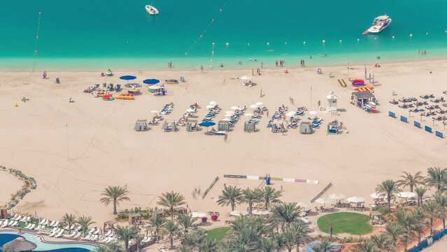 Crowded JBR beach with tourists enjoying the sun and the sea, sitting under umbrellas aerial top view from above timelapse