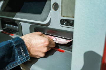 Obraz premium Close up of man taking cash from ATM with credit card or debit card. Man hand taking money from bank cash ATM machine. Close up. Cash point. Finance, transactions, money withdraw, currency concept