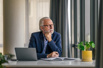 Thoughtful senior manager planning strategy while working on laptop at desk - obrazy, fototapety, plakaty