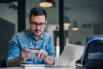 Young freelancer checking credit card while making online payment through laptop