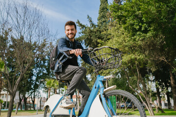 Handsome man looking to camera with smiling while on a rental bike ride on the city park on a sunny...