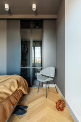 Stylish composition of modern bedroom interior. Wardrobe , grey chair and elegant personal accessories. Grey wall. Brown sheeets. Minimalistic masculine concept. Template.