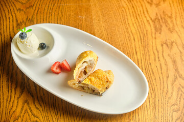 A piece of apple strudel with vanilla ice cream and strawberries