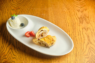 A piece of apple strudel with vanilla ice cream and strawberries