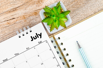 July 2022 desk calendar and open diary with pen on wooden background.
