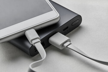 The smartphone is charging from external powerbank with cable. White background, closeup, selective focus