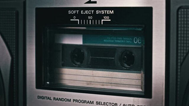 Audio cassette rotates in deck of old tape recorder. Audiocassette with blank label in retro player spinning and playing. Close-up. Retro call recording, playback, reel playing, vintage technology