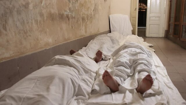 Man covered white sheet after murder of russian occupier, lot of corpses. Group of dead people lie on ground covered with white blanket. Feet are visible. Corpses on the floor