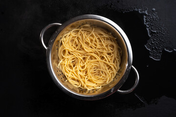 colander with cooked spaghetti on dark background