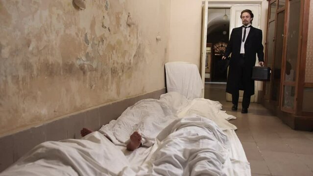 Man notices lot of dead people. Man covered white sheet after murder of russian occupier, lot of corpses. Group of dead people lie on ground covered with white blanket. Feet are visible. Corpses on