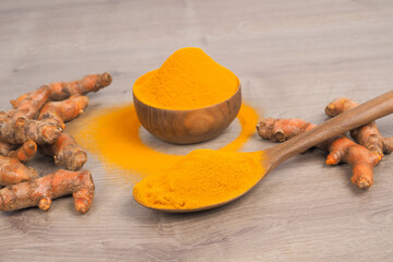 Turmeric powder and fresh turmeric in wooden spoon on old wooden table. Herbs are native to Southeast Asia.