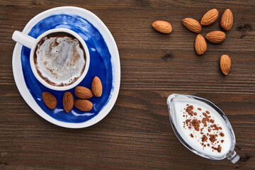 Cup of cappuccino almonds and milk in a glass milk jug on a dark wooden table