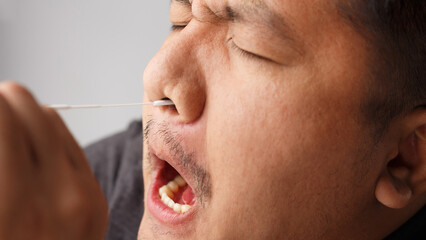 Asian men try to using Rapid Antigen Test Kit (ATK) by himself and painful emotion on his face