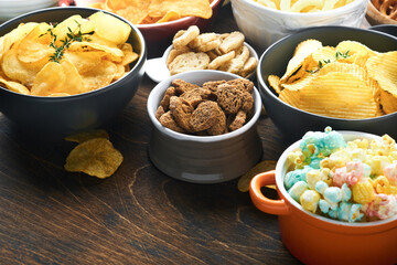 Unhealthy food or snacks. All classic potato snacks with peanuts, popcorn and onion rings and salted pretzels in bowl plates on old wooden background. Unhealthy food for figure, heart, skin, teeth.