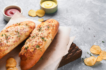 Baguette boats. Hot baked sandwich on baguette bread with ham, bacon, vegetables and cheese on parchment and wooden stand on gray concrete background. Top view. Copy space.
