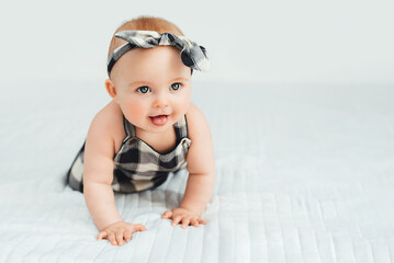 Cute smiling little baby girl sitting on bed. Seven month old infant child on grey soft blanket