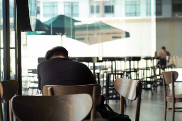 Rear view of thoughtful man sits alone on the high chair and works in the coffee shop with blurred people in background