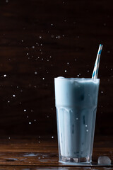Blue latte in a tall glass glass with two straws. The spray is flying up.