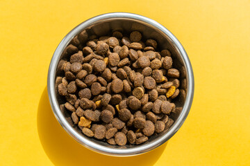Kibble in pet bowl on the yellow background, close up image