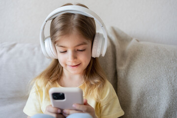 Happy girl with headphones sitting at home on the couch. The child is happy to learn at home online, listening to music playing games.