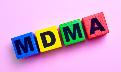 On a light pink background, multi-colored wooden cubes with the text MDMA