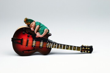 Newborn rests on a guitar in a green mohawk hat.