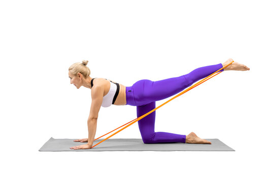 Glutes workout with resistance band. Caucasian athletic woman does kicks with straight leg on a mat standing on all fours, isolated on white.