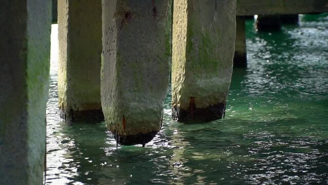 The destroyed pillars of the bridge stand in the sea. Pier on the ocean. concrete pillars are washed with water. Bridge in the ocean on the shore. Reinforcement in the supports is visible.