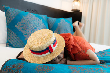 Woman in an orange hat is sleeping tired on the bed.