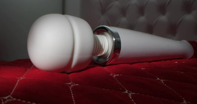 detailed, extreme close-up of a white vibrator on a bed with carriage tie on a red blanket