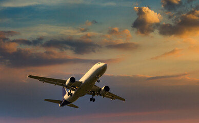 Passenger commercial aircraft flying under the clouds in sunset light.