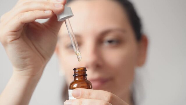 Close up of female young caucasian woman opens bottle with skin care oil dropper. Wellness and spa at home